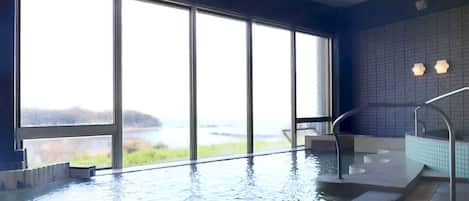 Una piscina interior con amplios ventanales que ofrecen vistas a un lago y colinas.