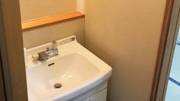 Une salle de bain avec un lavabo blanc, une étagère en bois au-dessus et des murs de couleur beige.
