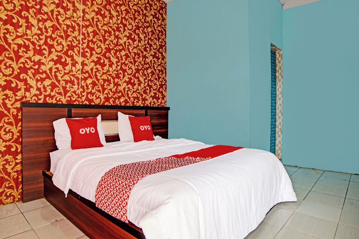 Una cama bien hecha con ropa de cama blanca y almohadas rojas, un cabecero de madera y una pared con estampado rojo y dorado.
