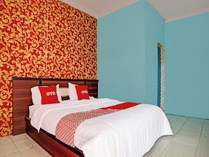 Una cama bien hecha con ropa de cama blanca y almohadas rojas, un cabecero de madera y una pared con estampado rojo y dorado.