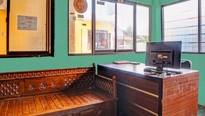 A reception desk with a computer, a wooden bench, and a wall-mounted fan. - Kantil Homestay Syariah (Medan)