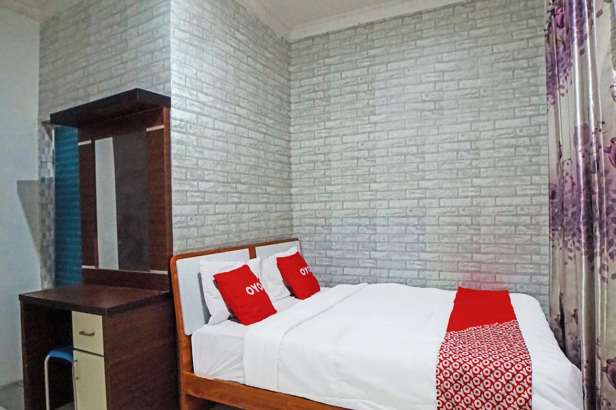 A bedroom with a wooden bed, white bedding, and red pillows. There is a wooden dresser with a mirror and a blue chair. The walls are covered with a brick-pattern wallpaper.