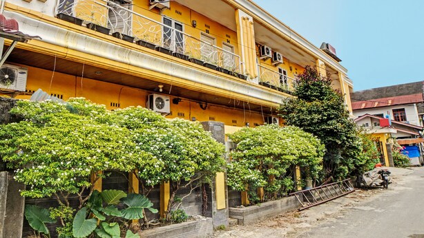 A multi-story yellow building with balconies, air conditioning units, and a tree in the foreground. - Kantil Homestay Syariah (Medan)