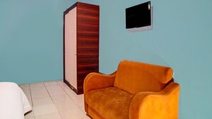A room with a blue wall, a wooden wardrobe, a small TV mounted on the wall, and a yellow sofa. - Kantil Homestay Syariah (Medan)