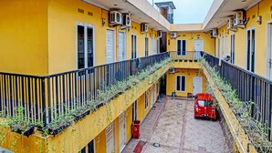A yellow building with balconies, air conditioning units, and a red car parked in the courtyard. - Kantil Homestay Syariah (Medan)