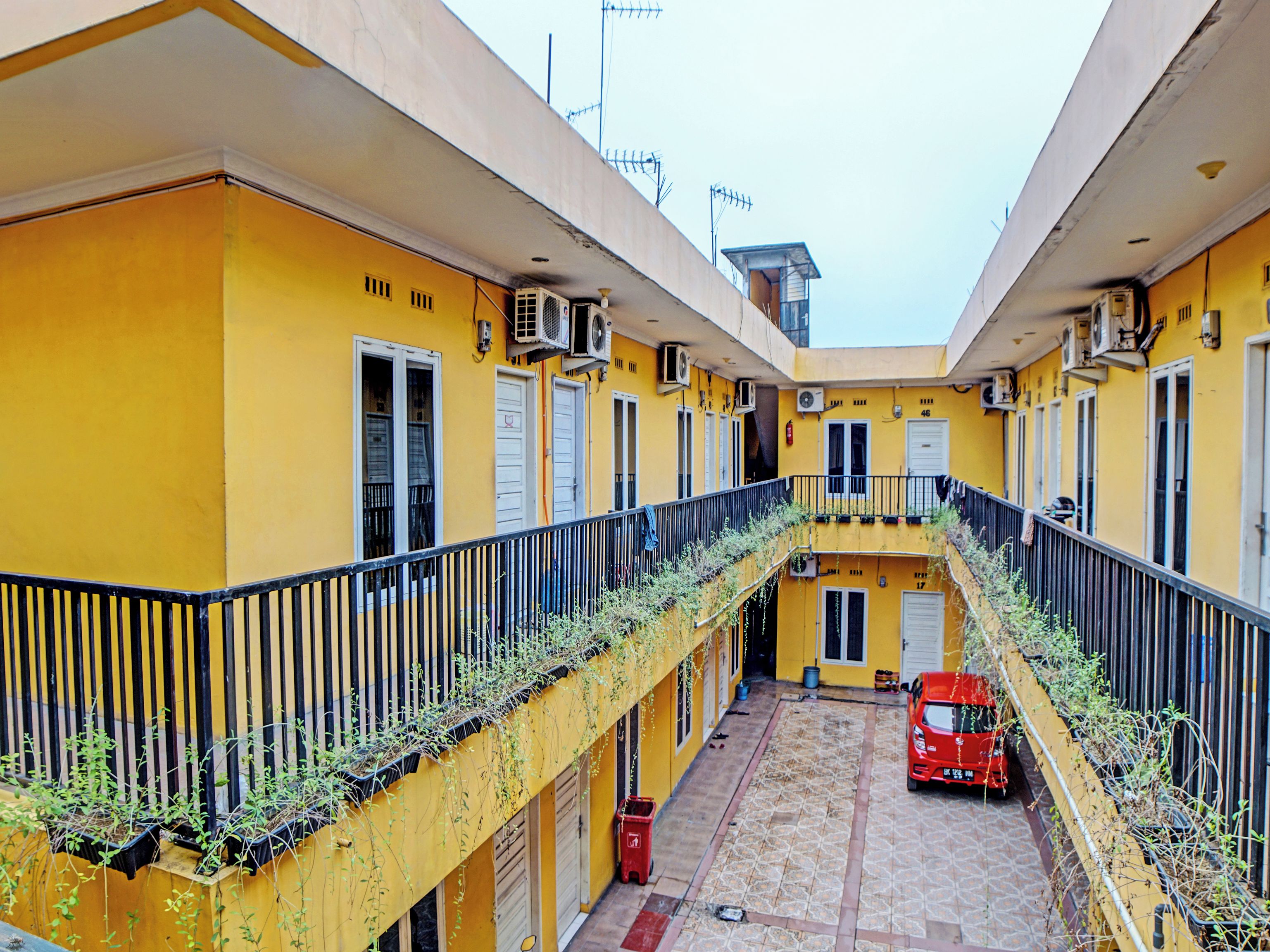 A yellow building with multiple balconies, a red car parked in the courtyard, and a tiled floor.