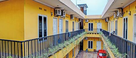 A yellow building with multiple balconies, a red car parked in the courtyard, and a tiled floor.