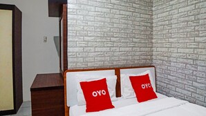 A bedroom with a brick-patterned wall, a wooden headboard, and two red pillows with the word "OYO" on them. - Kantil Homestay Syariah (Medan)
