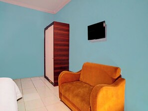 Een kamer met een oranje bank, een kledingkast en een wandtelevisie.