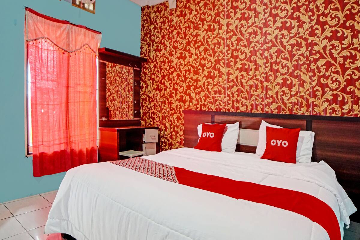 A hotel room with a bed, a nightstand, a mirror, and a window with curtains.