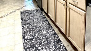 Una cucina moderna con mobili in legno chiaro, un piano di lavoro in granito nero e un tappeto decorato.