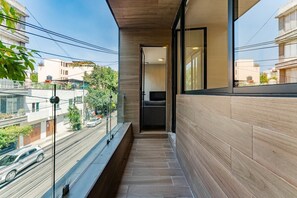Uma varanda estreita com chão de madeira, uma porta de vidro que dá para um quarto e vista para a rua abaixo.