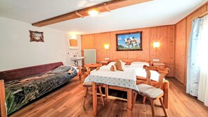 A cozy room with wooden walls, a dining table with chairs, a sofa, and a bed.