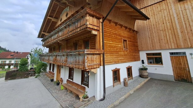 A traditional wooden chalet with a balcony, stone steps, and a stone wall.