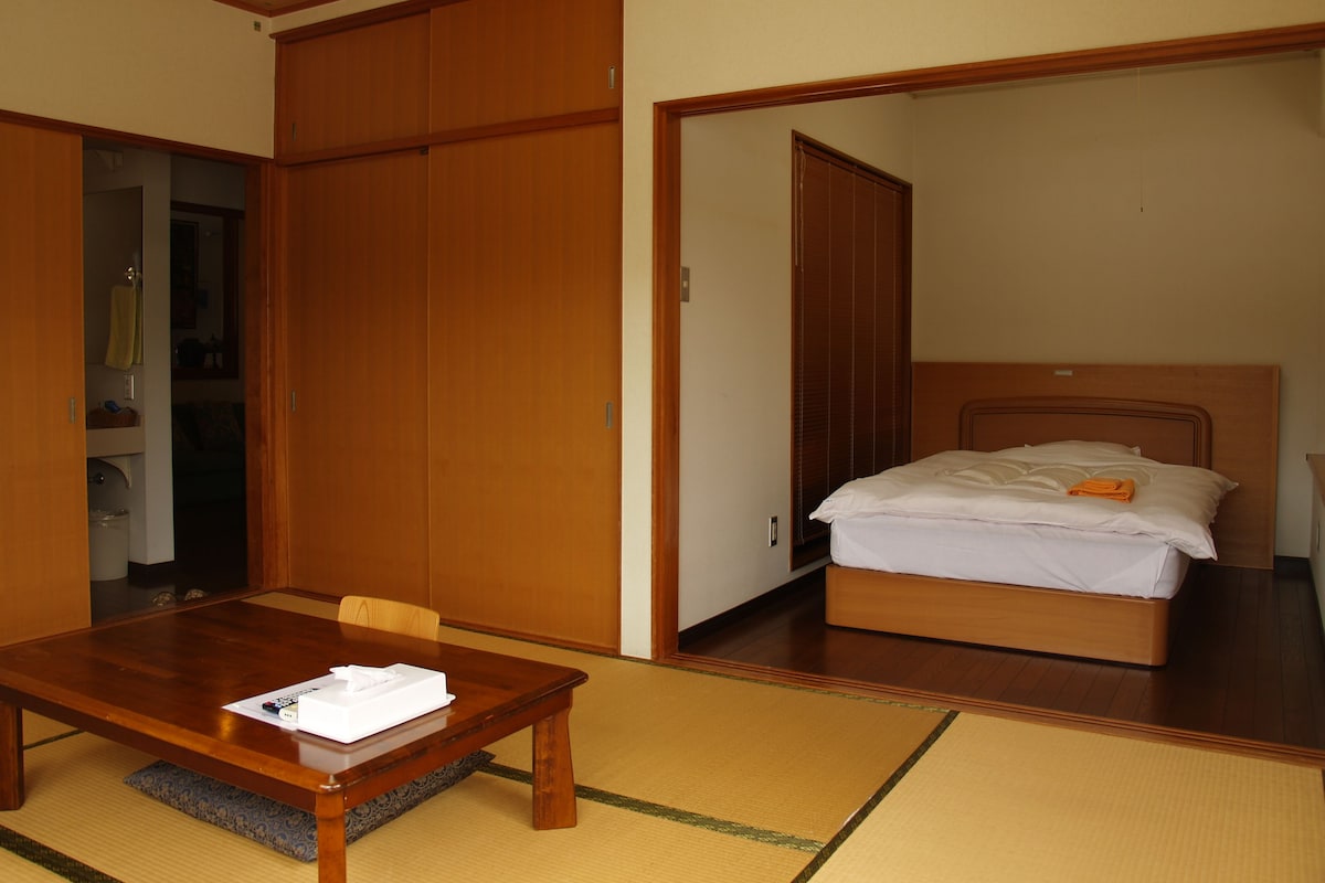A hotel room with a wooden bed, a wooden table, and a tatami mat floor.
