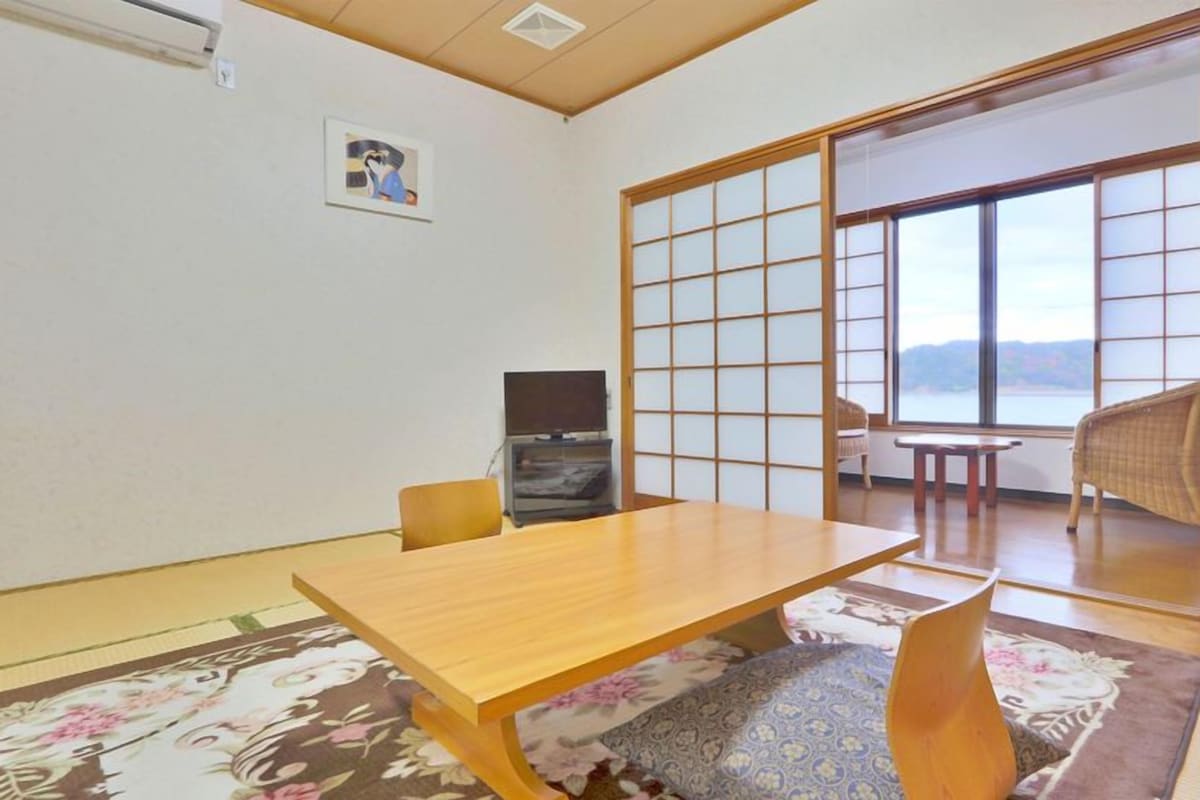 A traditional Japanese room with tatami flooring, a low wooden table, a television, and a sliding shoji screen.