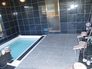 A modern bathroom with a rectangular pool, dark tiled walls, and wooden stools.