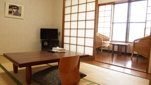 A traditional Japanese room with tatami flooring, a low wooden table, a television, and a sliding door leading to a balcony with wicker furniture. - Guesthouse Amy Monbos (Higashikagawa)