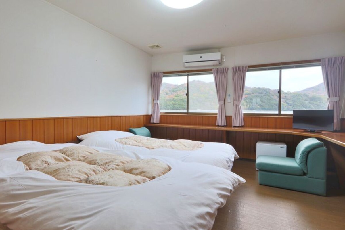 A hotel room with two beds, a television, a desk, and a window with curtains.