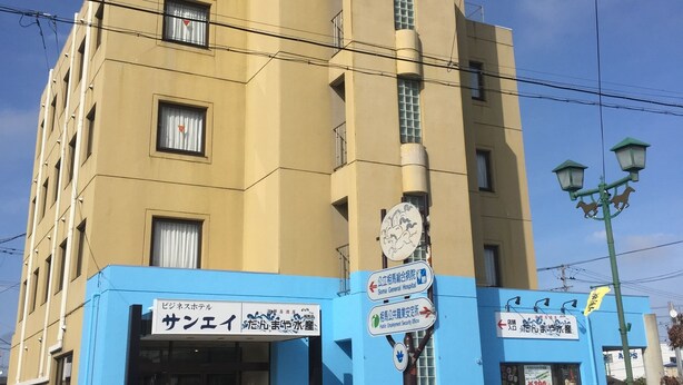 Un edificio de varios pisos con fachada azul y color crema, que muestra señalización para un hotel y una oficina de seguridad social.