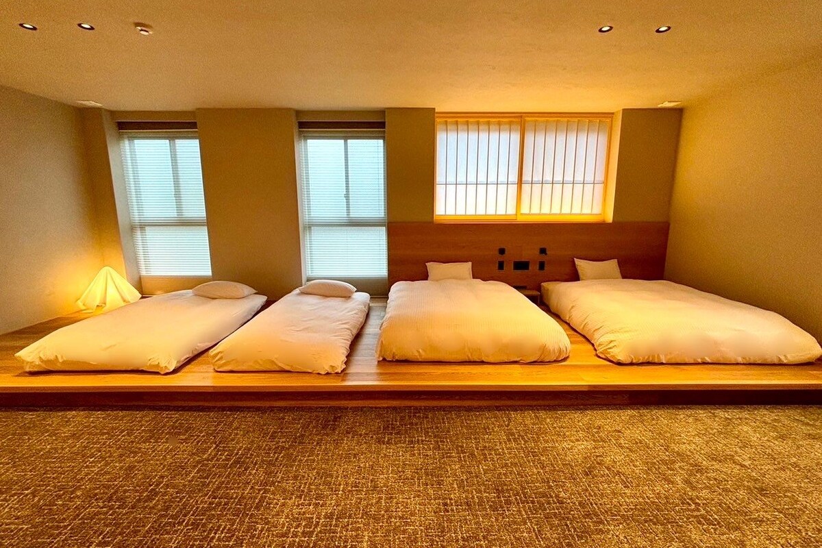Una habitación de hotel con una cama grande, dos ventanas y suelo alfombrado.