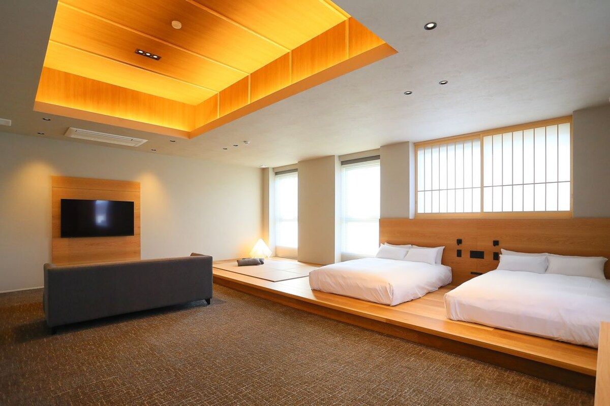 A modern hotel room with a large bed, a sofa, a TV, and a wooden ceiling design.