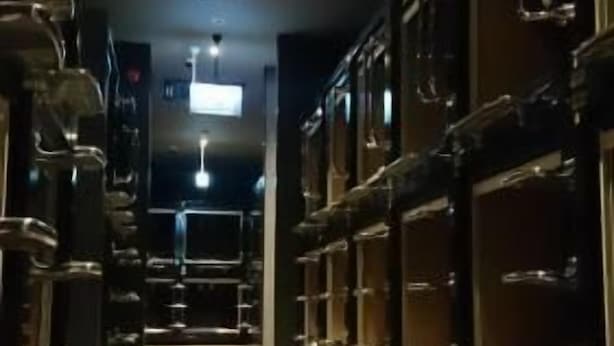 Un pasillo de hotel con alfombra estampada, taquillas de metal y un respiradero en el techo.