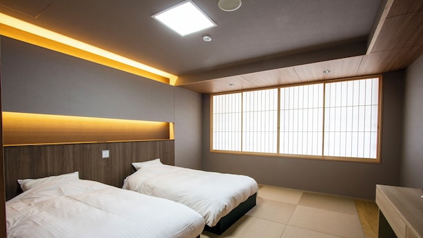 A modern hotel room with two beds, a large window with vertical blinds, and a wooden headboard. - Okuizumocho Cycling Terminal (Okuizumo)