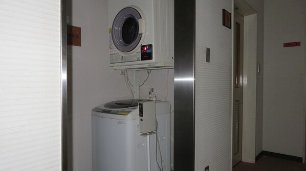 Habitación de hotel con lavadora, un estante pequeño con un reloj y una puerta con un letrero rojo.