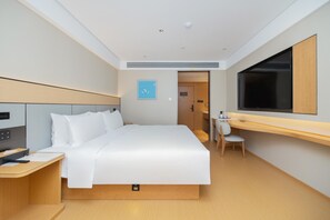 A hotel room with a bed, a desk, a chair, a TV, and a door.