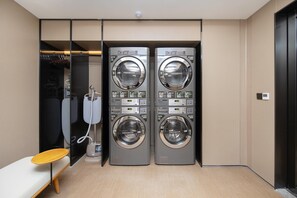 A modern laundry room with two wall-mounted washing machines, a telephone, and a wooden bench. - Ji Hotel Guangzhou Sun Yat-sen University (Guangzhou)