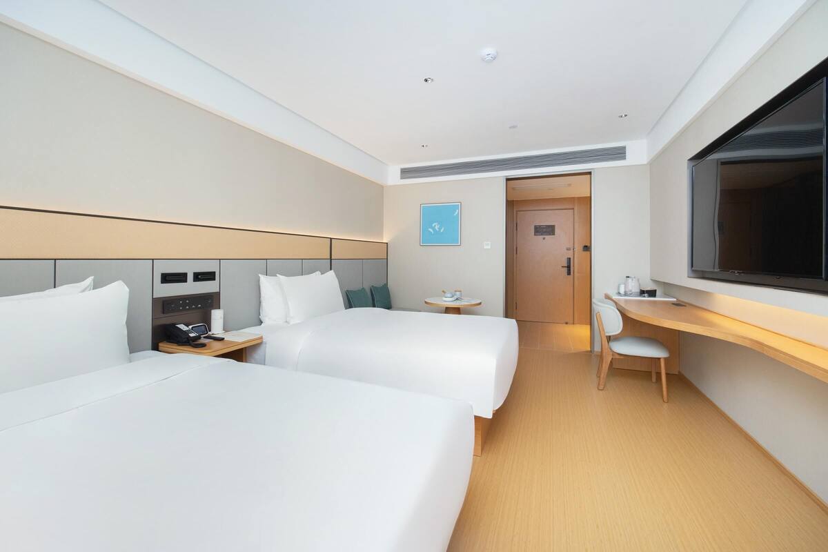 A hotel room with two beds, a desk, a chair, a TV, and a small table with a phone and a cup.