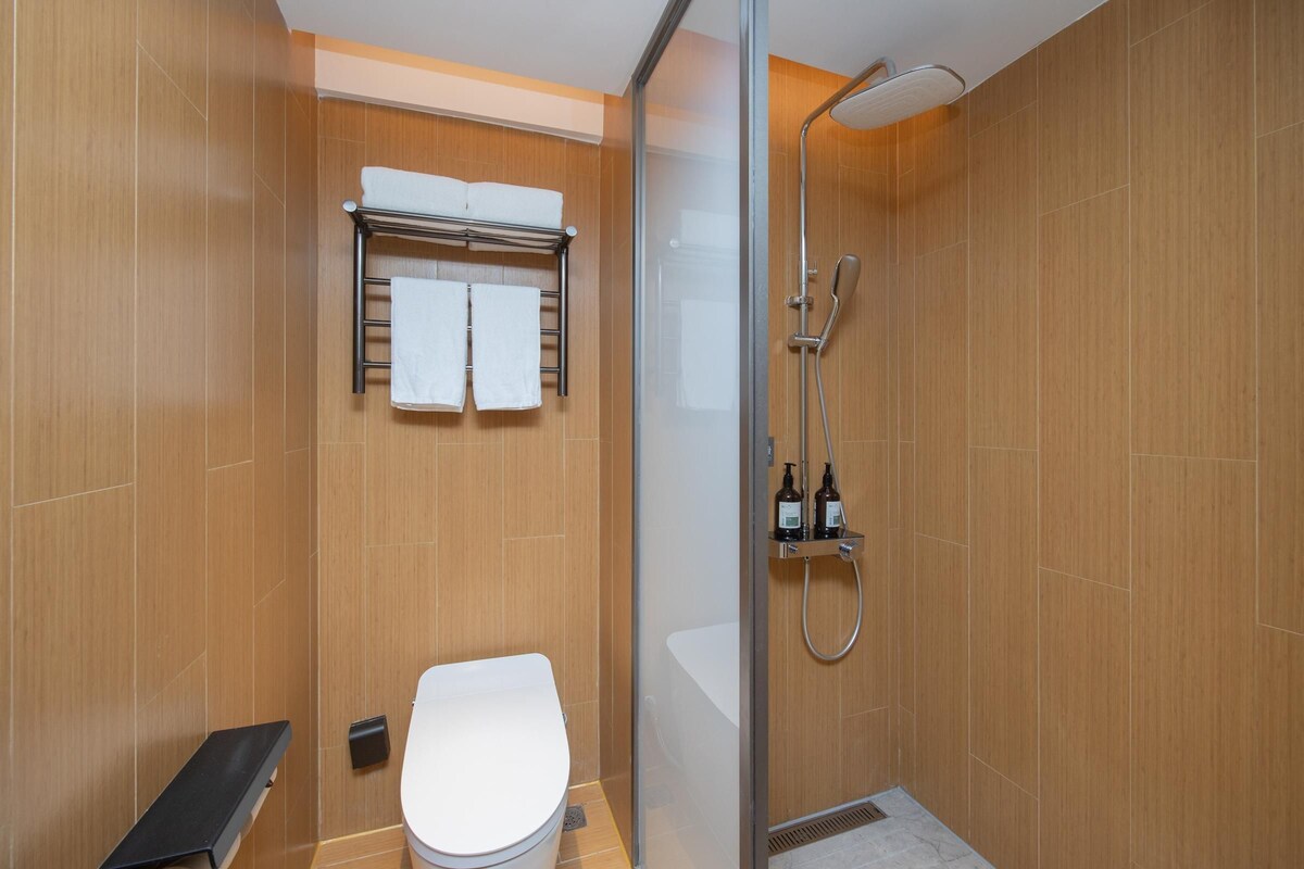 A modern bathroom with a glass shower enclosure, a toilet, and a towel rack with two towels.