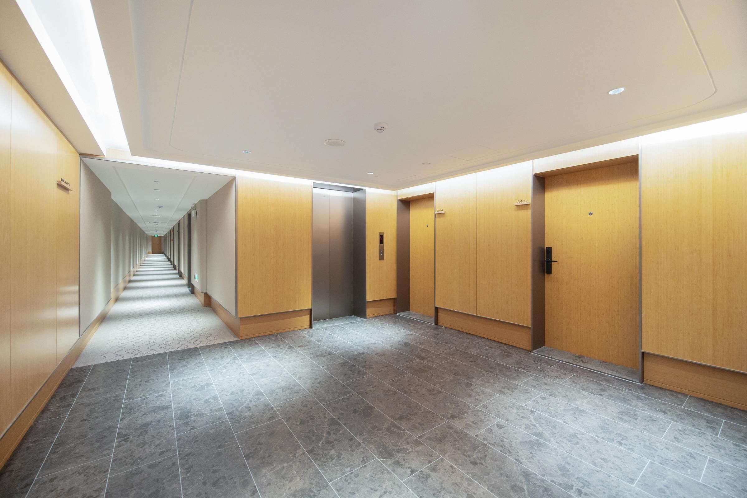 A modern hallway with a tiled floor, wooden doors, and a central elevator.