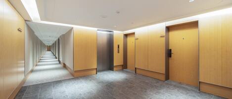 A modern hallway with a tiled floor, wooden doors, and a central elevator.