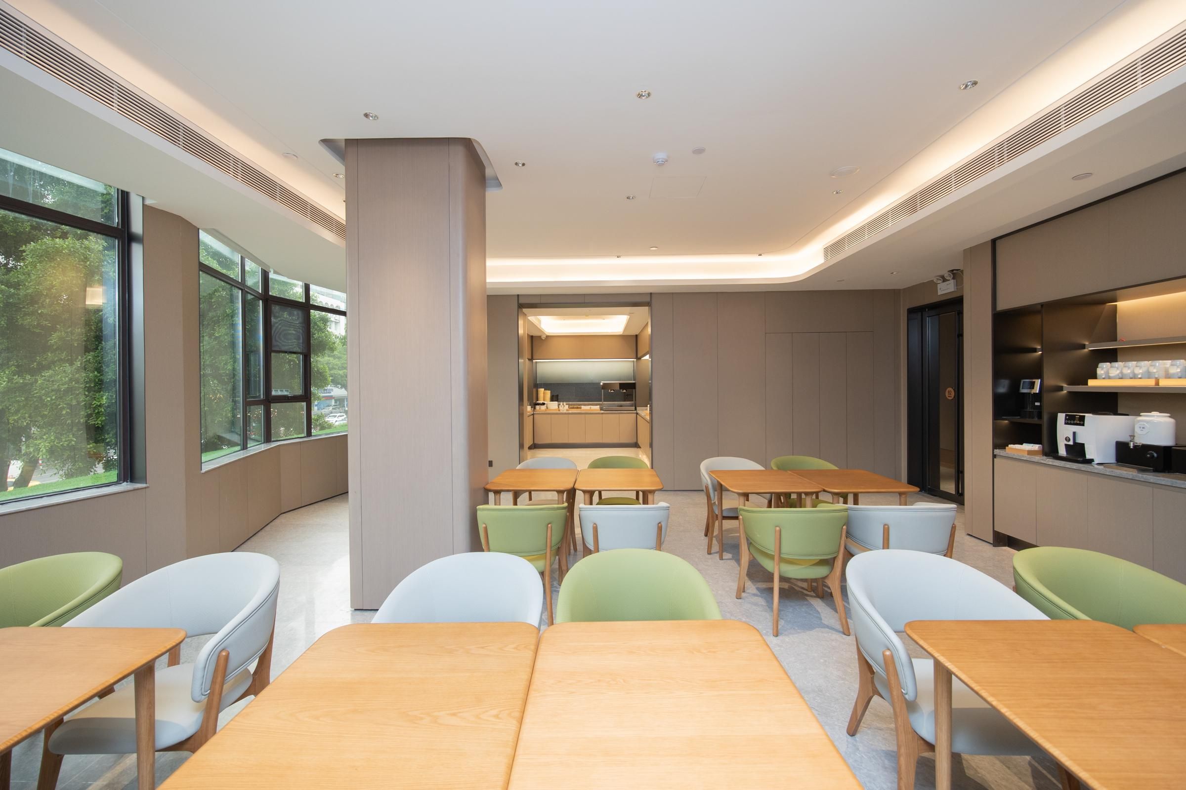 Un espace repas moderne avec des tables et des chaises, de grandes fenêtres et une cuisine en arrière-plan.