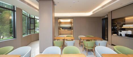 A modern dining area with tables and chairs, large windows, and a kitchen in the background.