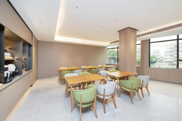 Un espace repas moderne avec des tables et des chaises, une machine à café et de grandes fenêtres.