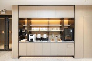 A modern kitchenette with built-in appliances, including a coffee machine, tea maker, and a refrigerator.