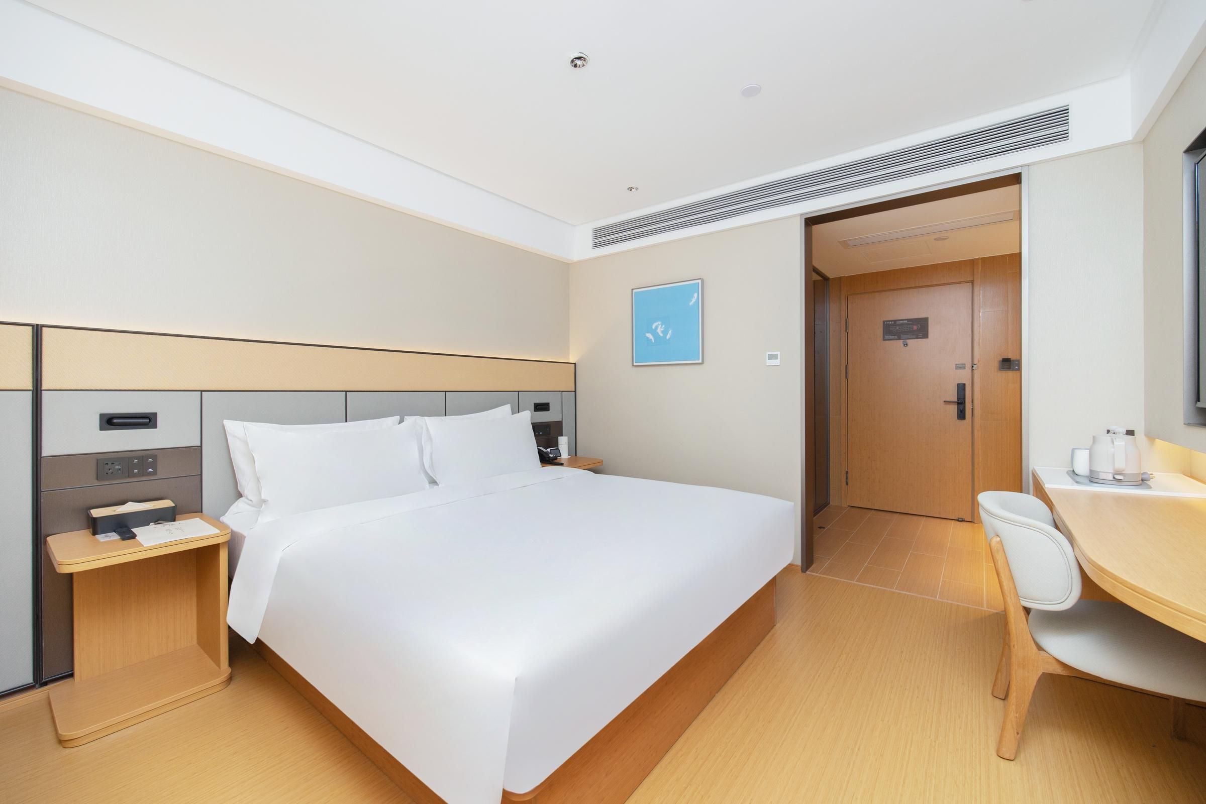 A hotel room with a bed, bedside table, desk, chair, and a door.