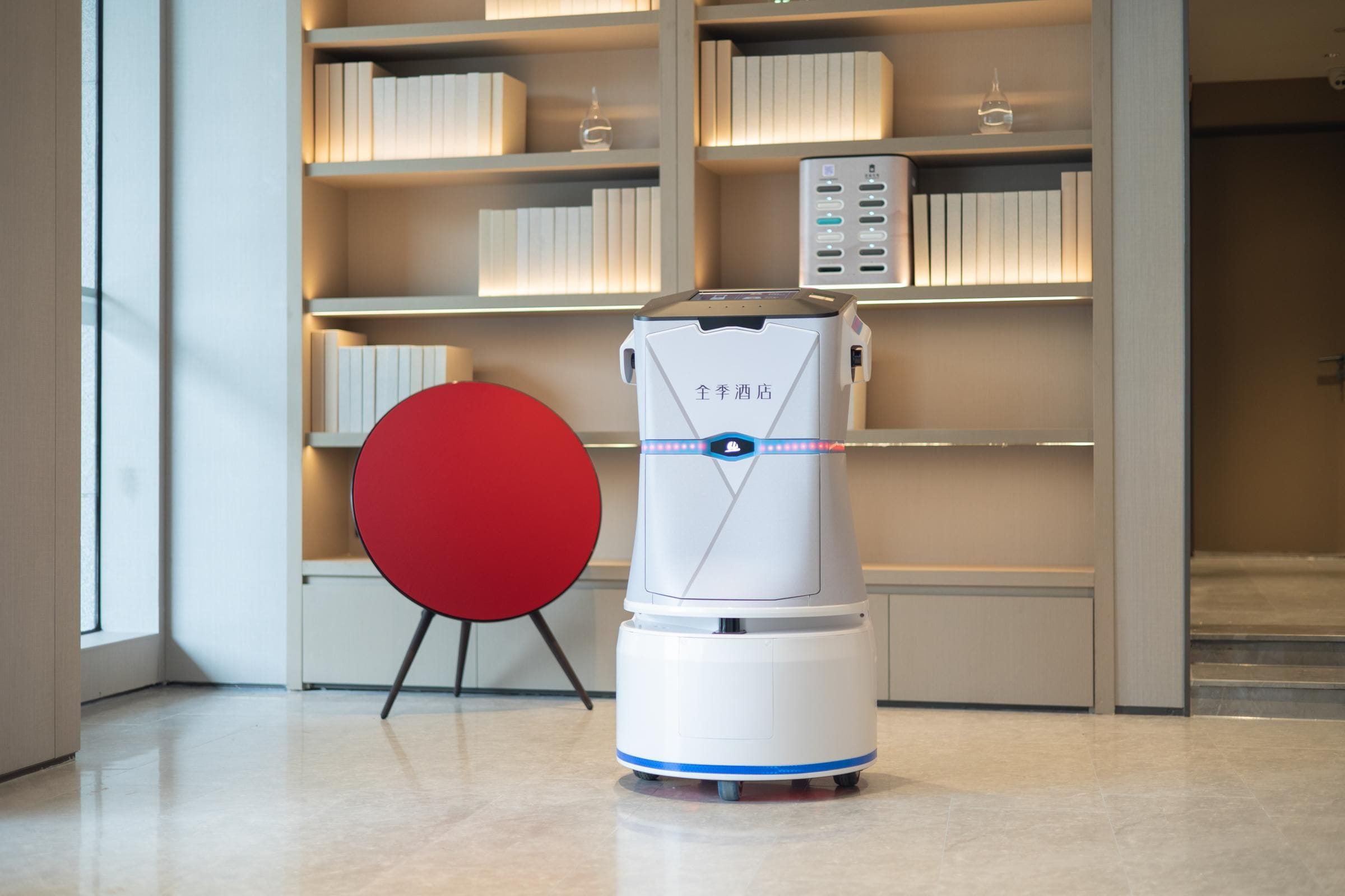 Un robot en un moderno vestíbulo de hotel con una estantería y una silla roja.