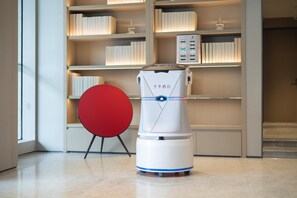 A robot in a modern hotel lobby with a bookshelf and a red chair. - Ji Hotel Guangzhou Sun Yat-sen University (Guangzhou)