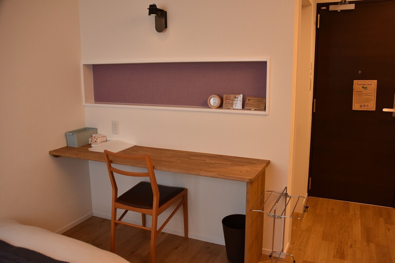 A small room with a wooden desk, a chair, a shelf with items, and a door with an ecology card.