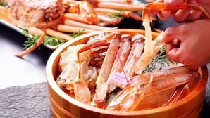 A wooden bowl filled with cooked shrimp, a person holding a shrimp, and a plate with more shrimp in the background. - Sekinoya (Kami)
