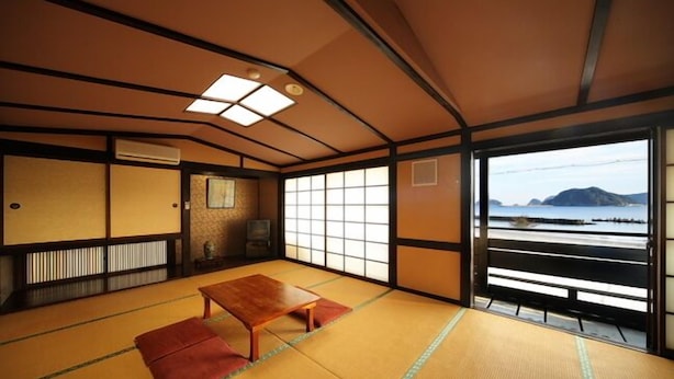 A traditional Japanese room with tatami flooring, a low table, sliding doors, and a view of the sea. - Sekinoya (Kami)