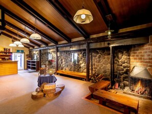A cozy interior with a stone fireplace, wooden benches, and a reception desk. - Community House Tyrolien (Hakuba)