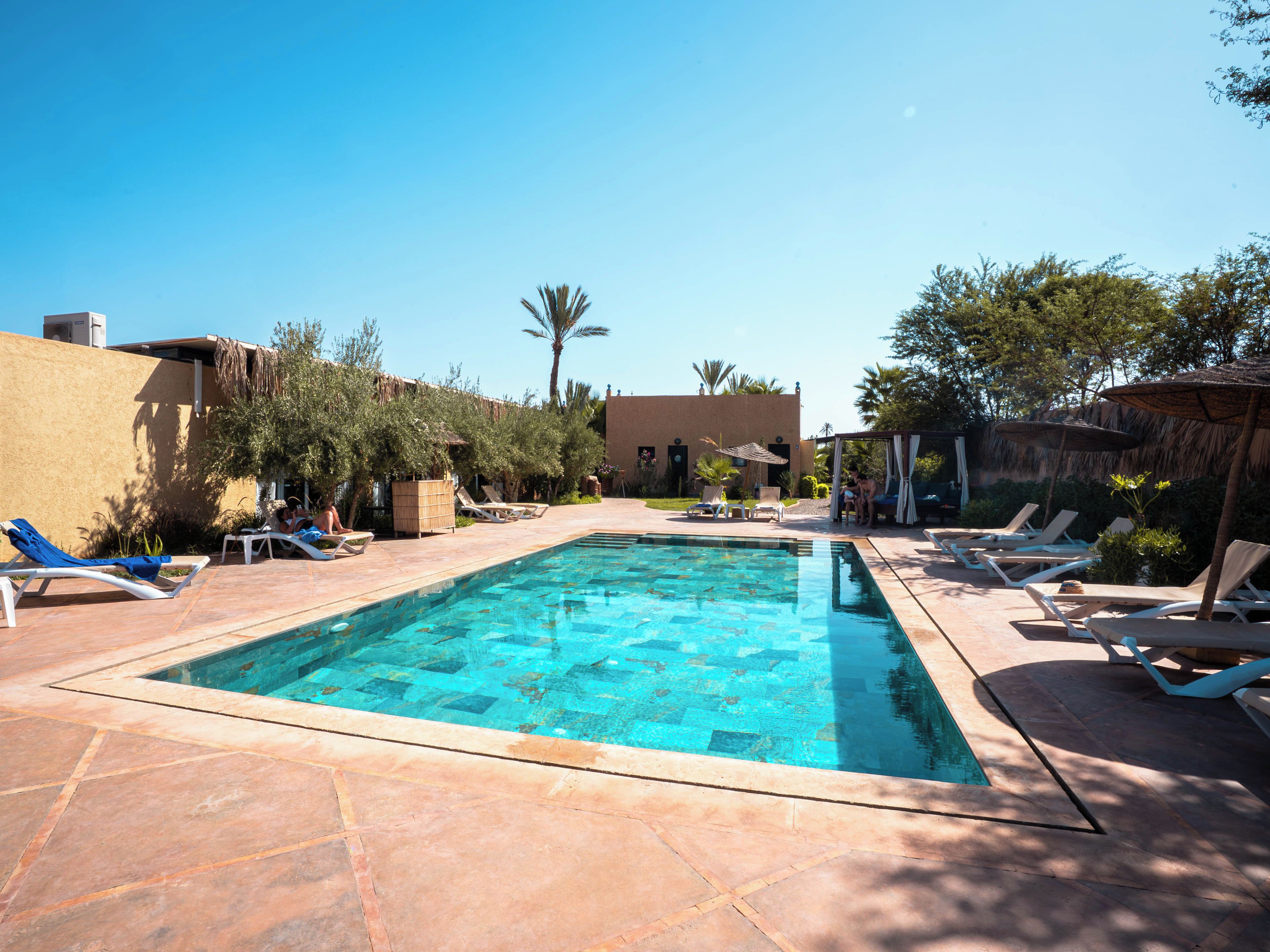 A swimming pool with lounge chairs and umbrellas, surrounded by vegetation and buildings.