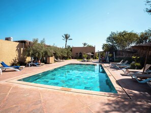 A swimming pool with lounge chairs and umbrellas, surrounded by vegetation and buildings. - Maison Daouia (Marrakech)