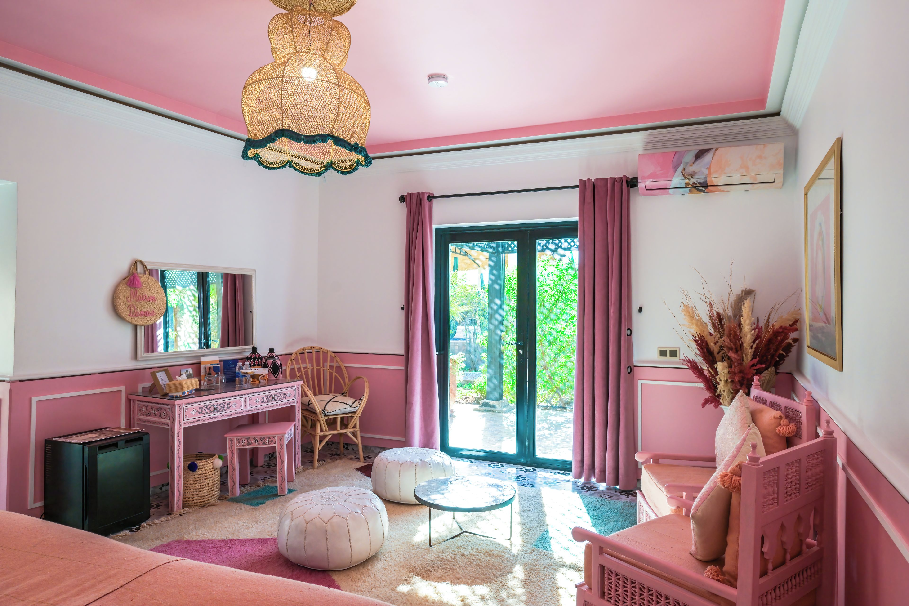 Una habitación decorada en tonos rosados, con escritorio, silla, reposapiés y cama.