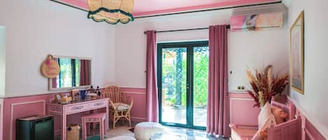 Una habitación decorada en tonos rosados, con escritorio, silla, reposapiés y cama.